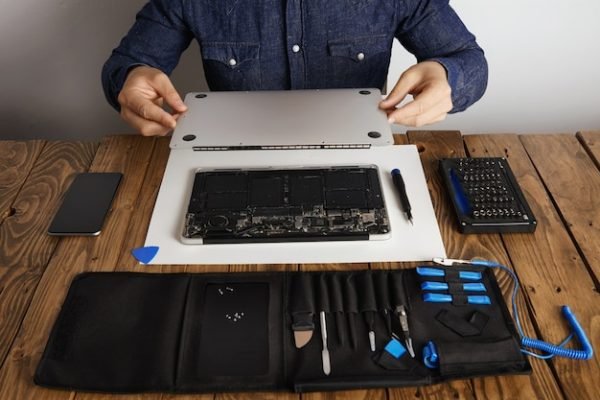 service-man-opens-backside-topcase-cover-computer-laptop-before-repairing-cleaning-fixing-it-with-his-professional-tools-from-toolkit-box-near-wooden-table-front-view_346278-1799